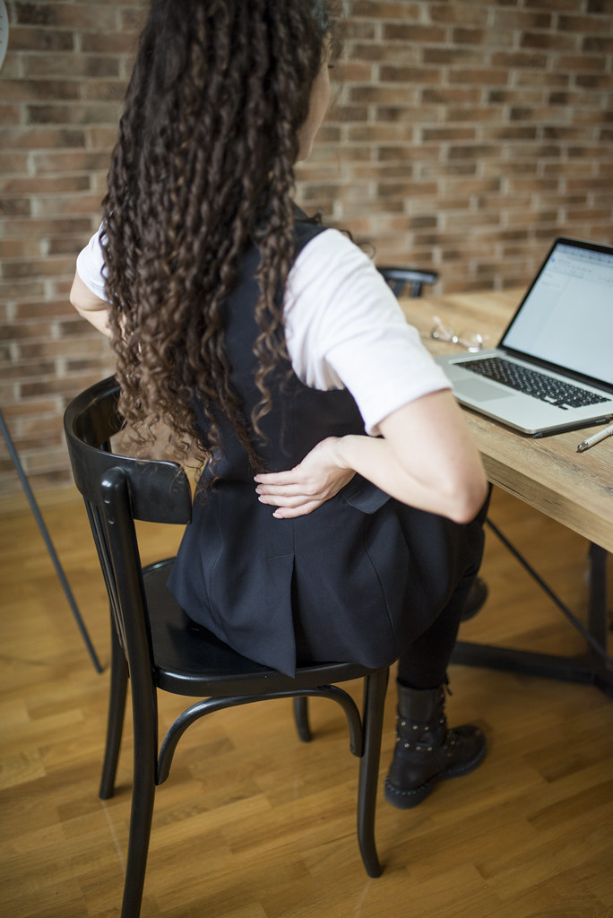 A young woman having back pain while sitting at the desk in her office
